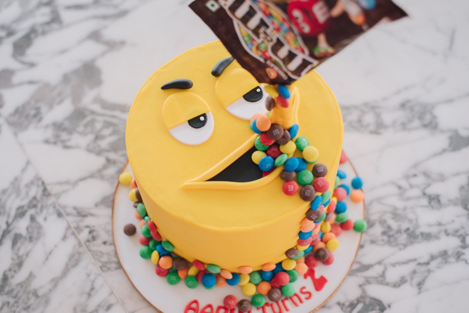 Best 10 Place To Customize your Own Cakes in Egypt M&M pack pouring candies on M&m cake's mouth on marble surface