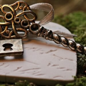 A vintage key with an intricate design rests on a heart-shaped keepsake amidst green moss.