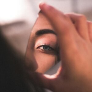 You Don’t Need to Fix Him: Why the Savior Complex Is Wrecking Your Relationships A captivating image of a woman's eye reflected in a broken mirror piece with soft lighting.