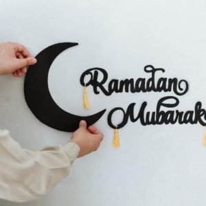 Close-up of hands hanging a Ramadan Mubarak sign with a crescent moon on a wall, signifying festive decoration.