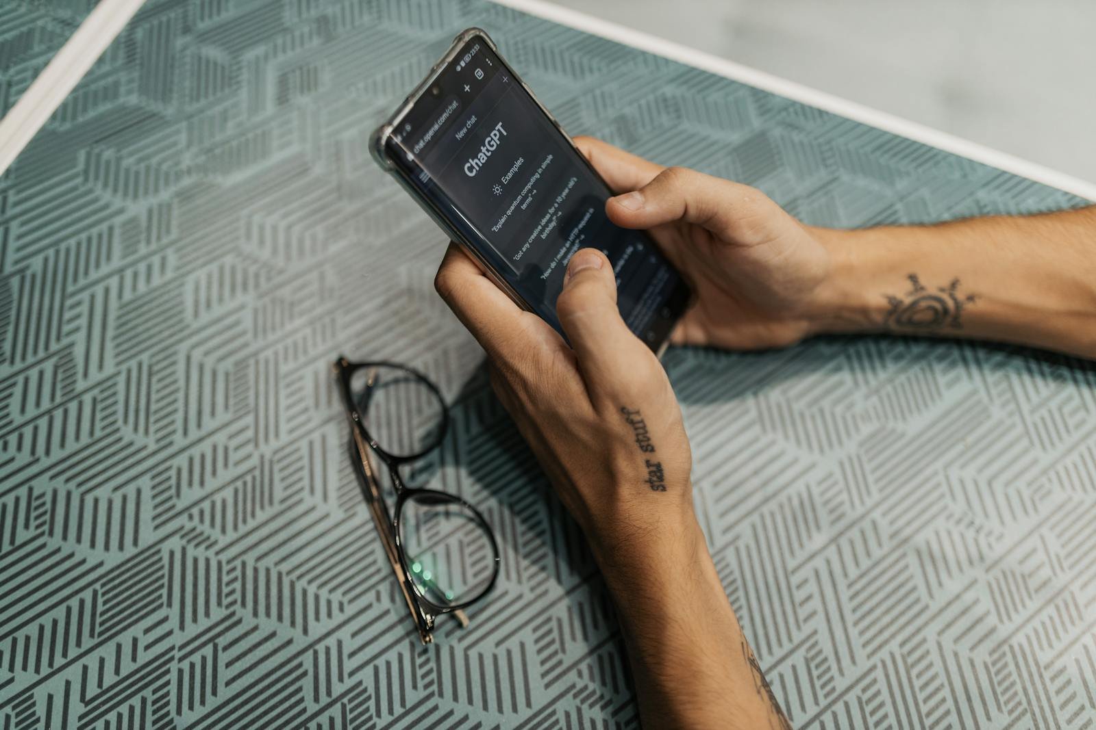 Close-up of a person holding a smartphone showing the ChatGPT app next to eyeglasses.